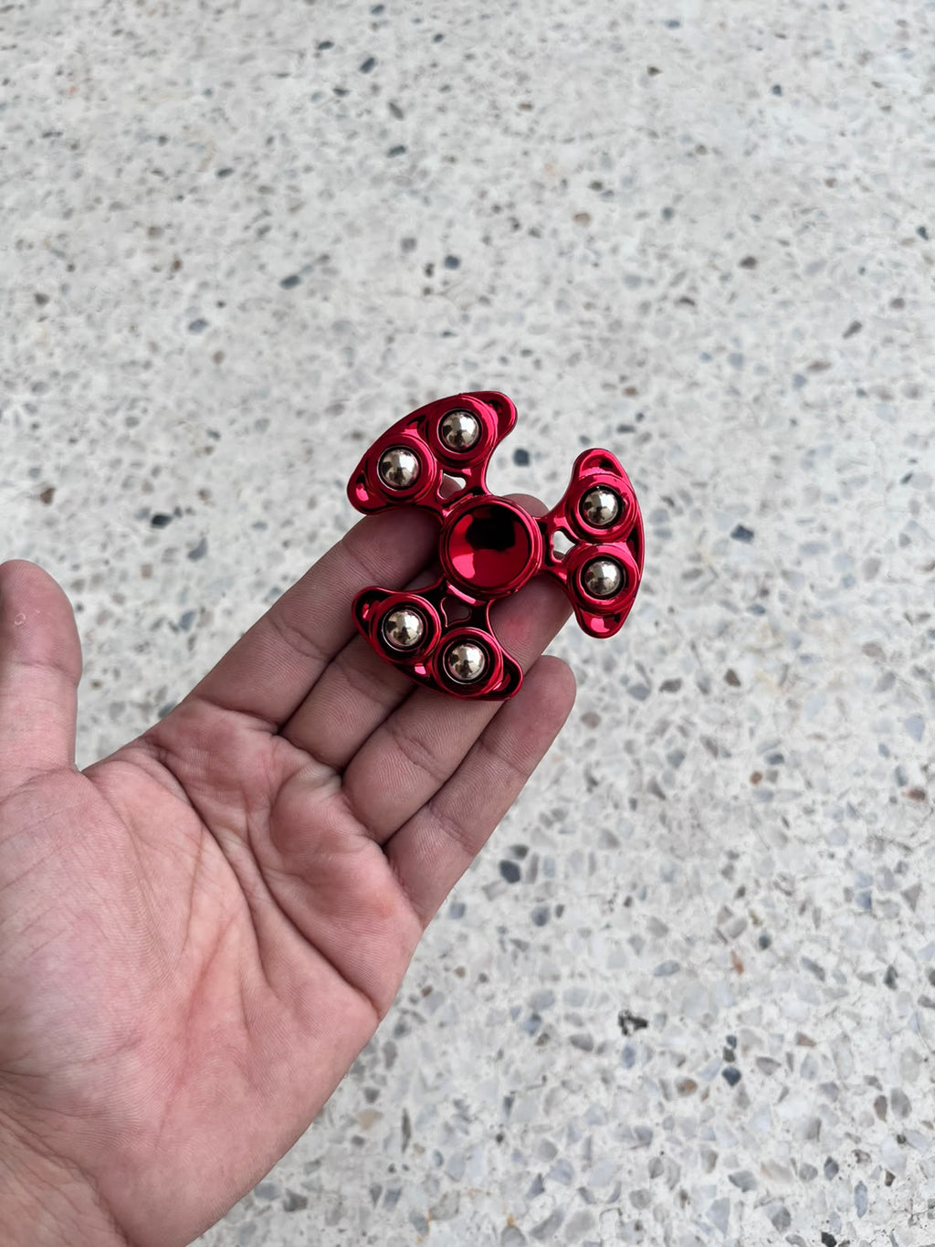 Red three-arm fidget spinner with six silver-coloured balls held in a hand