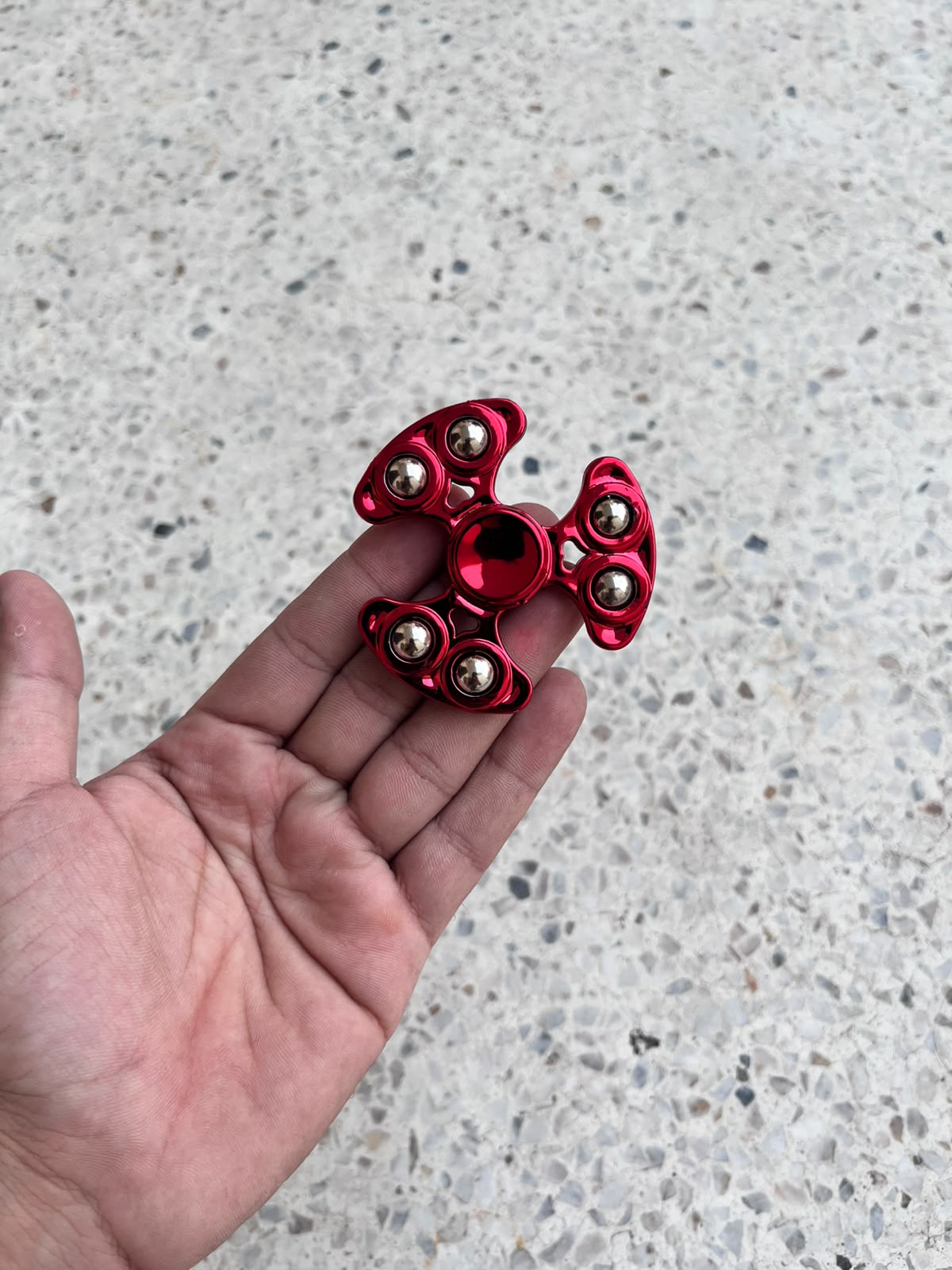 Red three-arm fidget spinner with six silver-coloured balls held in a hand