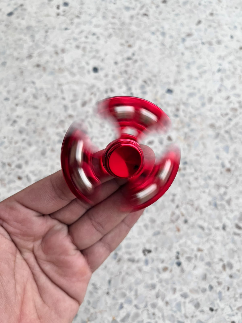 Angled view of a red fidget spinner spinning while held by its centre cap