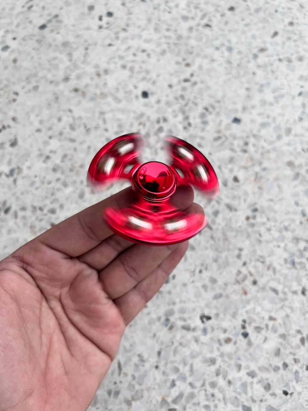 Red fidget spinner rotating between fingers with blurred arms
