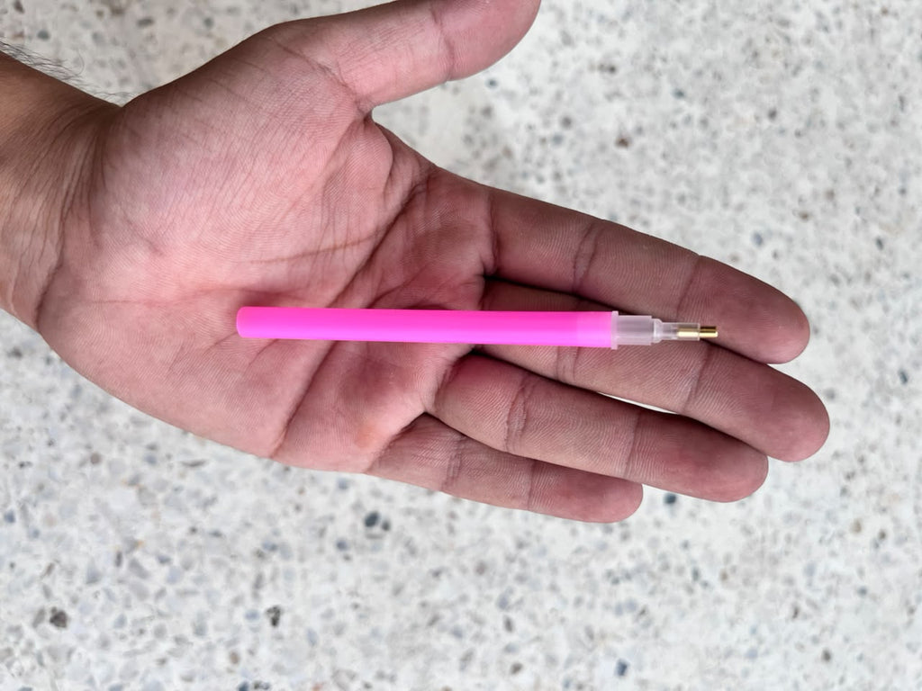 Pink diamond painting applicator pen with a narrow metal tip resting on a palm