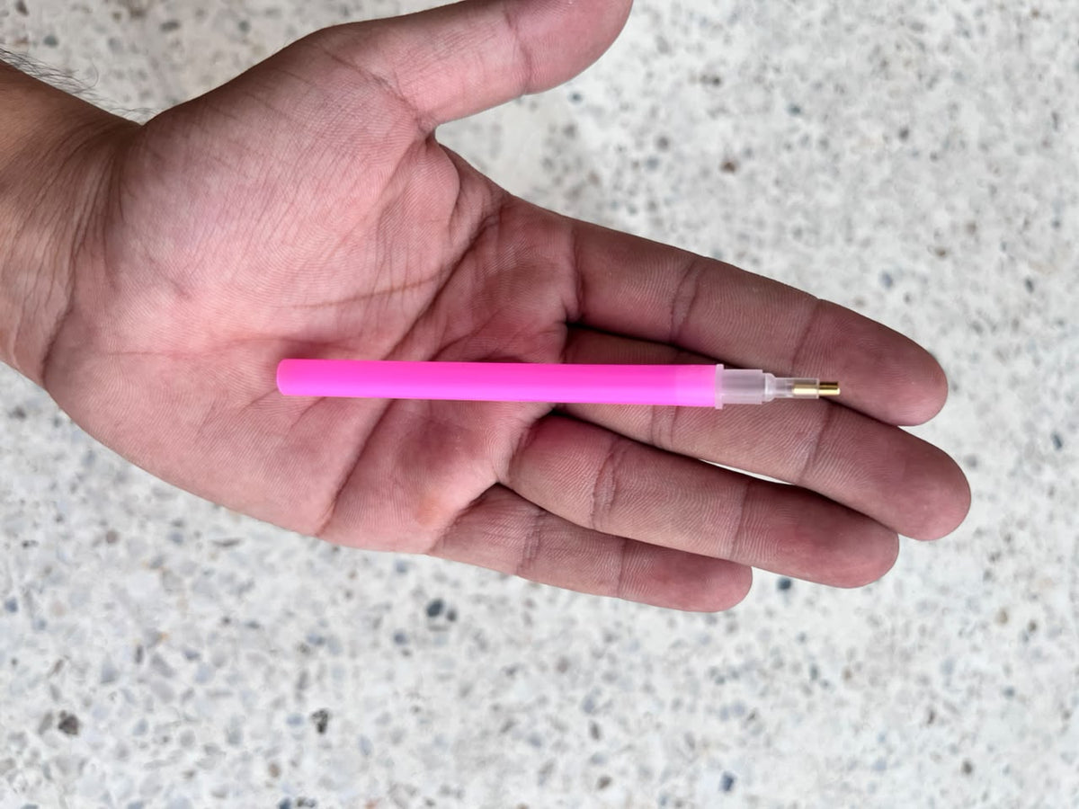 Pink diamond painting applicator pen with a narrow metal tip resting on a palm